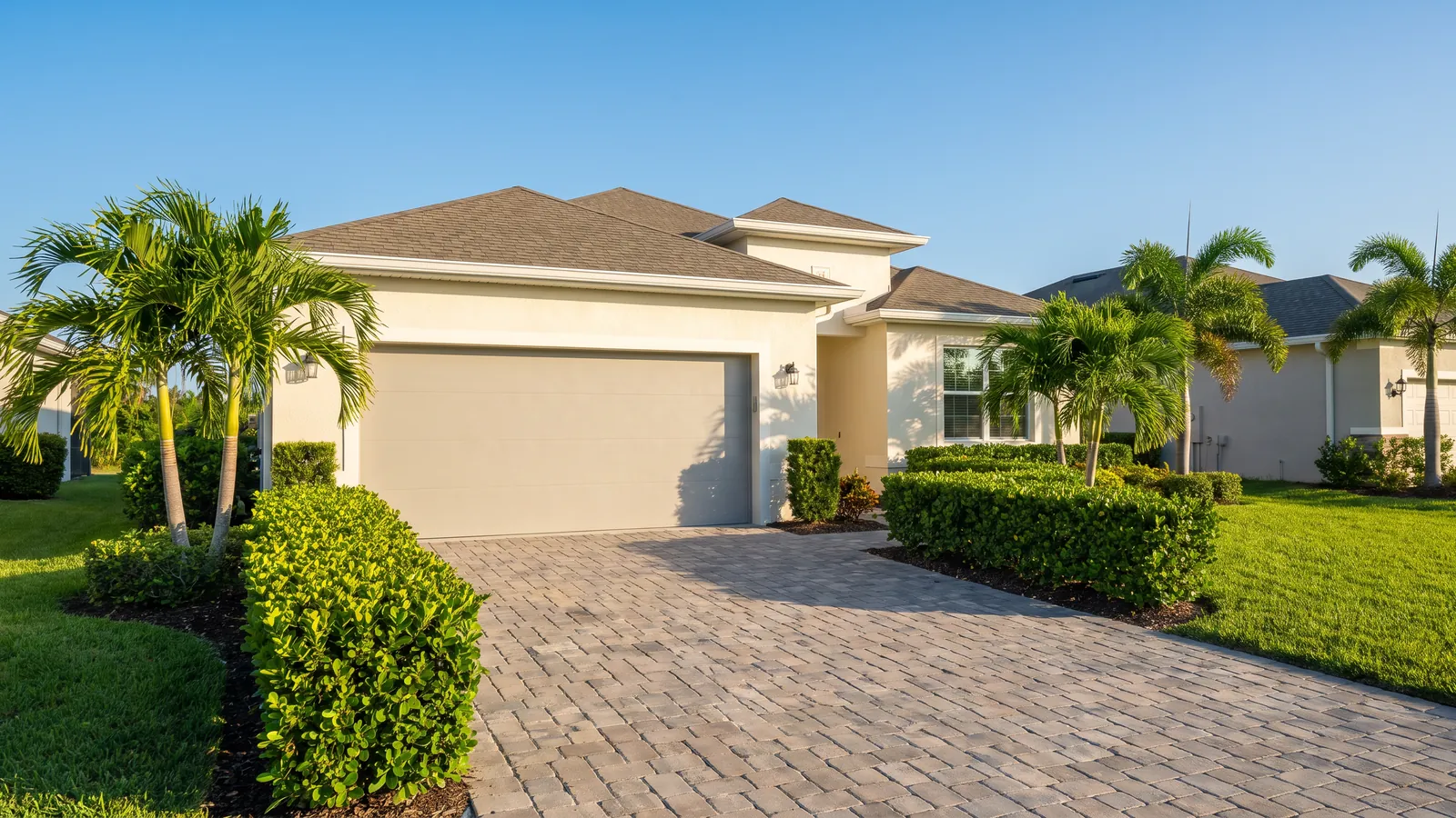 New flush-panel insulated steel garage door in a soft gray on a stucco home in a newer Port St. Lucie neighborhood, paver drive and clipped hedges